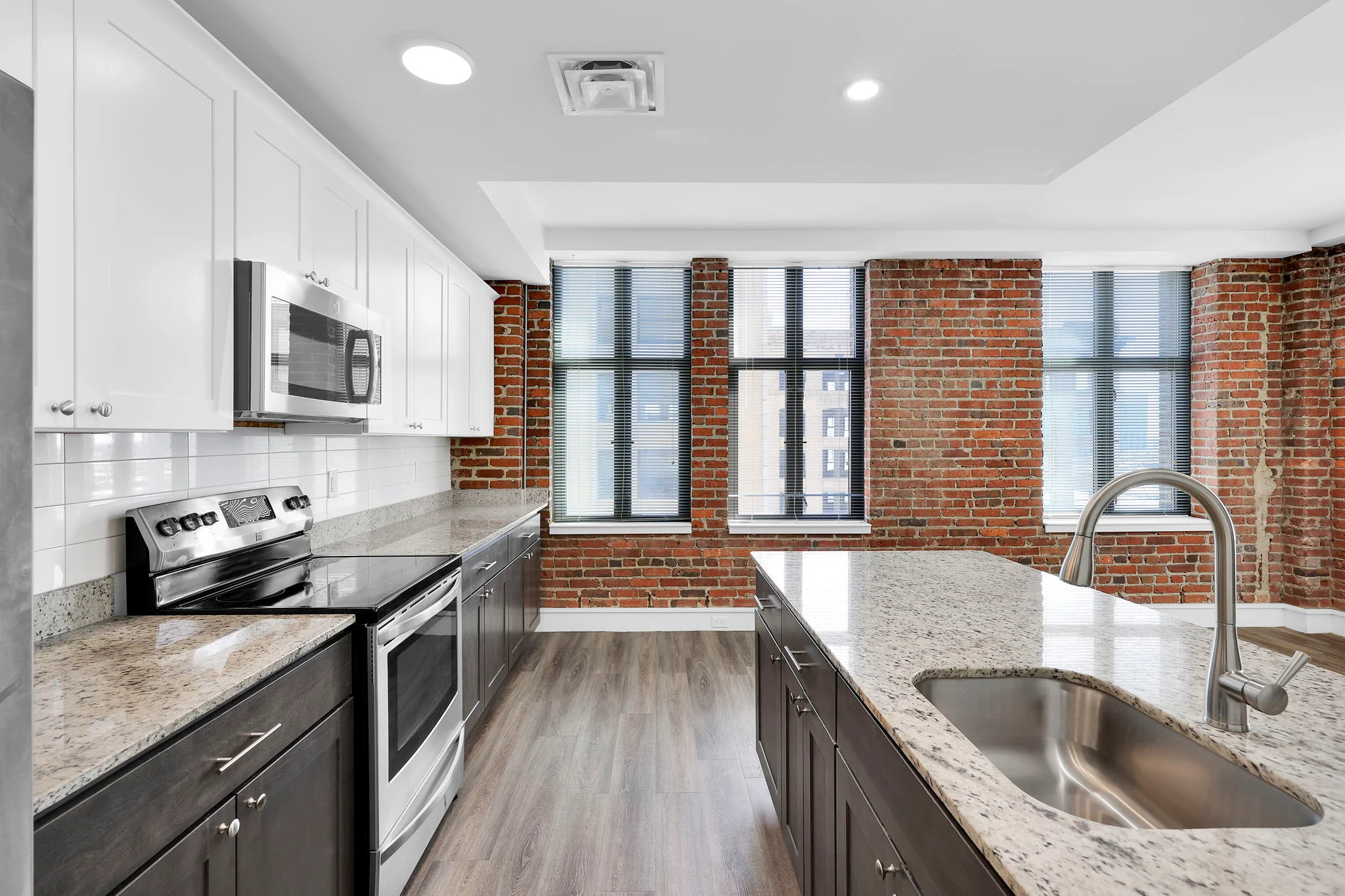Stylish Modern Kitchen Design A modern kitchen featuring white and dark cabinets, stainless steel appliances, and a granite countertop, with brick walls and large windows allowing natural light in.
