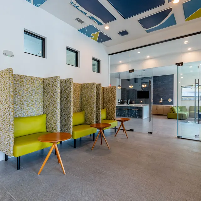 A modern lobby featuring spacious seating areas with high-backed chairs and small wooden tables, large windows, and a contemporary design on the ceiling.