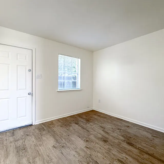An empty room featuring a wooden floor and white walls, with a door and a window.