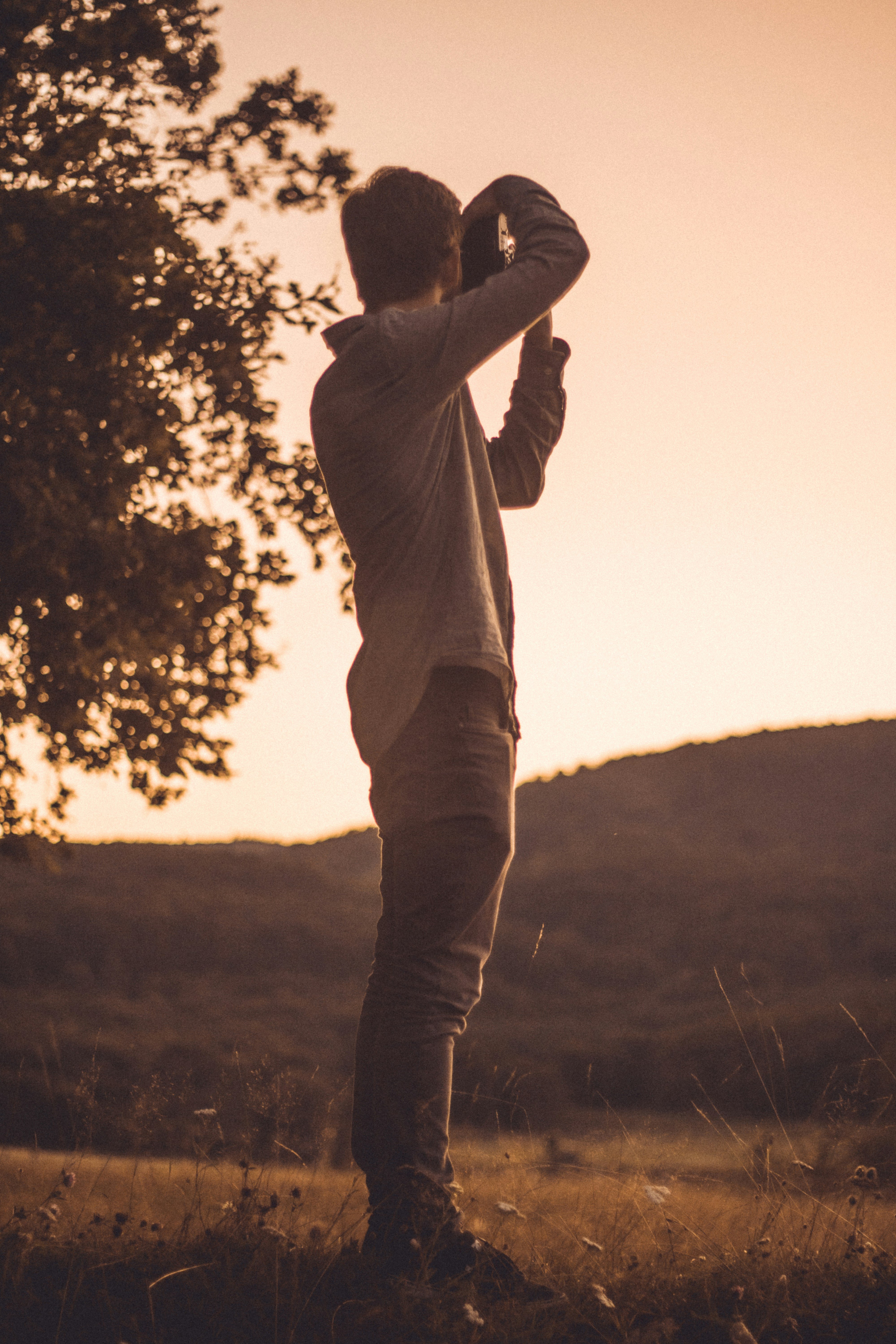 Silhouette of a person taking photos at sunset with a mountain in the background.
