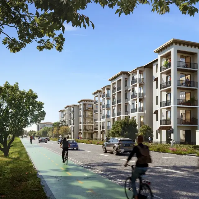 Modern Residential Development A modern residential area featuring several buildings along a tree-lined street with a bike lane. Bicyclists and cars are visible on the road, alongside green spaces.
