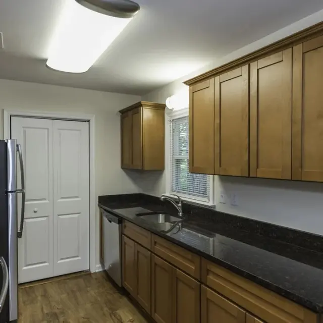 A modern kitchen featuring wooden cabinets, black granite countertops, stainless steel appliances, and a window providing natural light.