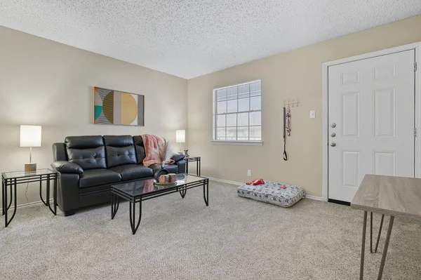 A modern living room featuring a black sectional sofa with cushions, a glass coffee table, two lamps, and light-colored walls.