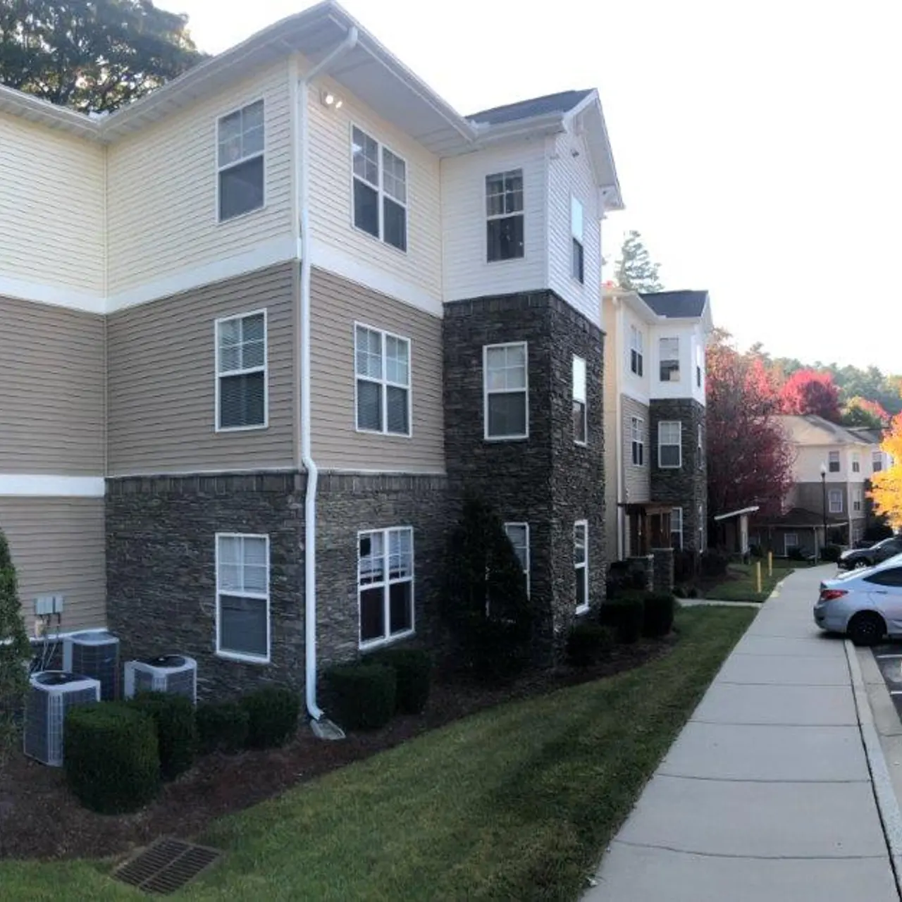 Exterior view of a modern apartment complex featuring brick and siding, with green landscaping and trees in autumn colors.