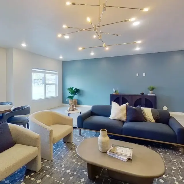 A spacious modern living room featuring a blue accent wall, a stylish light fixture, and contemporary furniture including a sofa, armchairs, and a coffee table.