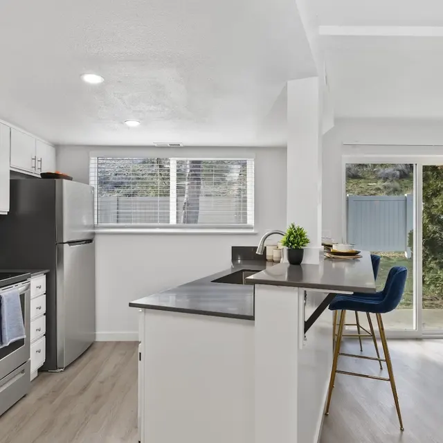 Monterra Townhomes - Modern Kitchen Interior A modern kitchen featuring white cabinetry, stainless steel appliances, and a spacious layout that opens to a living area with large sliding glass doors.