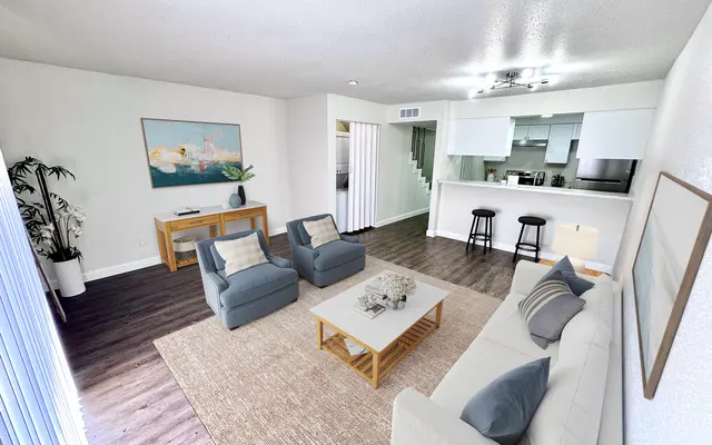 Modern Living Room Interior A bright and modern living room featuring a comfortable sofa, two armchairs, and a coffee table. There is an artwork on the wall, a plant in a corner, and a view into an adjacent kitchen area with bar stools.