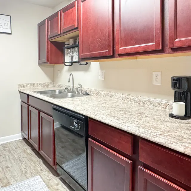 A modern kitchen featuring dark wood cabinets, a granite countertop, and stainless steel appliances. There is a small sink and a coffee maker on the countertop.