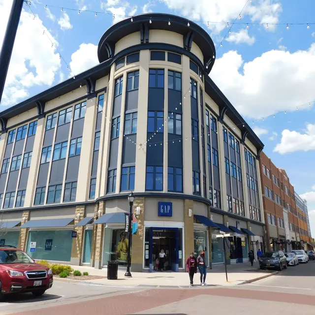 A modern multi-story building with a Gap store on the ground floor, surrounded by a busy street and other commercial buildings.