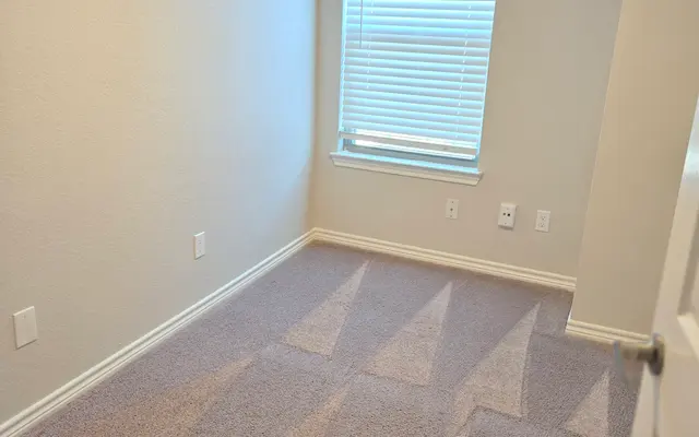 Empty Room with Window A sparsely furnished empty room with light-colored walls, a window covered with blinds, and carpet flooring.
