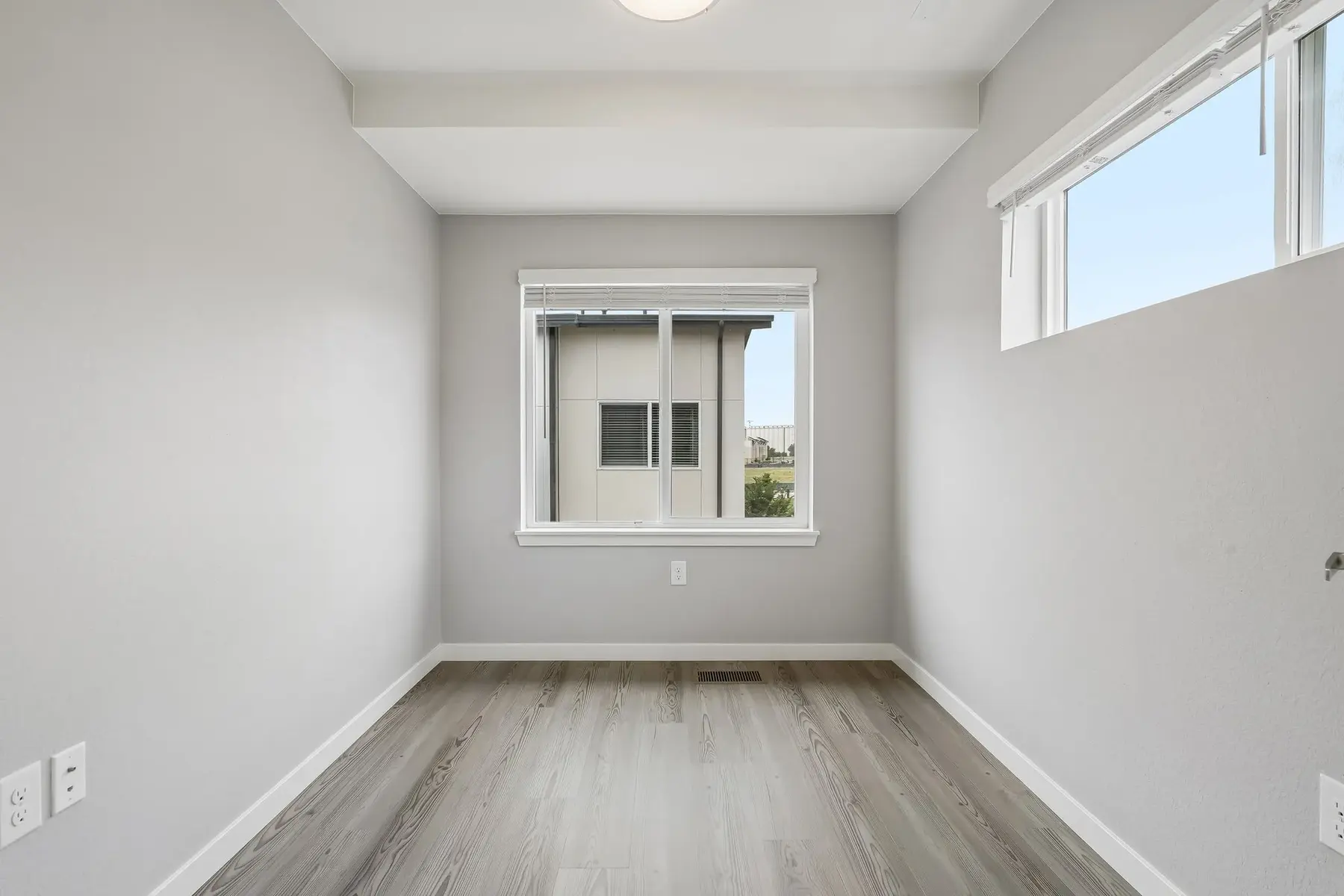 Empty Room with Natural Light A minimalist empty room with gray walls and wooden flooring, featuring large windows allowing natural light.