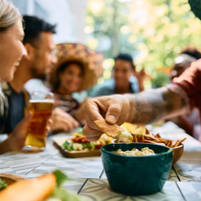 A group of friends gathered around a table enjoying food and drinks, with a variety of dishes and beverages visible.
