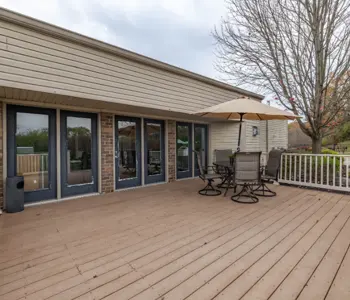Spacious outdoor patio area with a table and chairs under an umbrella, adjacent to a house with large windows.