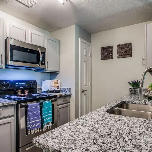 A modern kitchen featuring grey cabinets, stainless steel appliances, and a granite countertop.