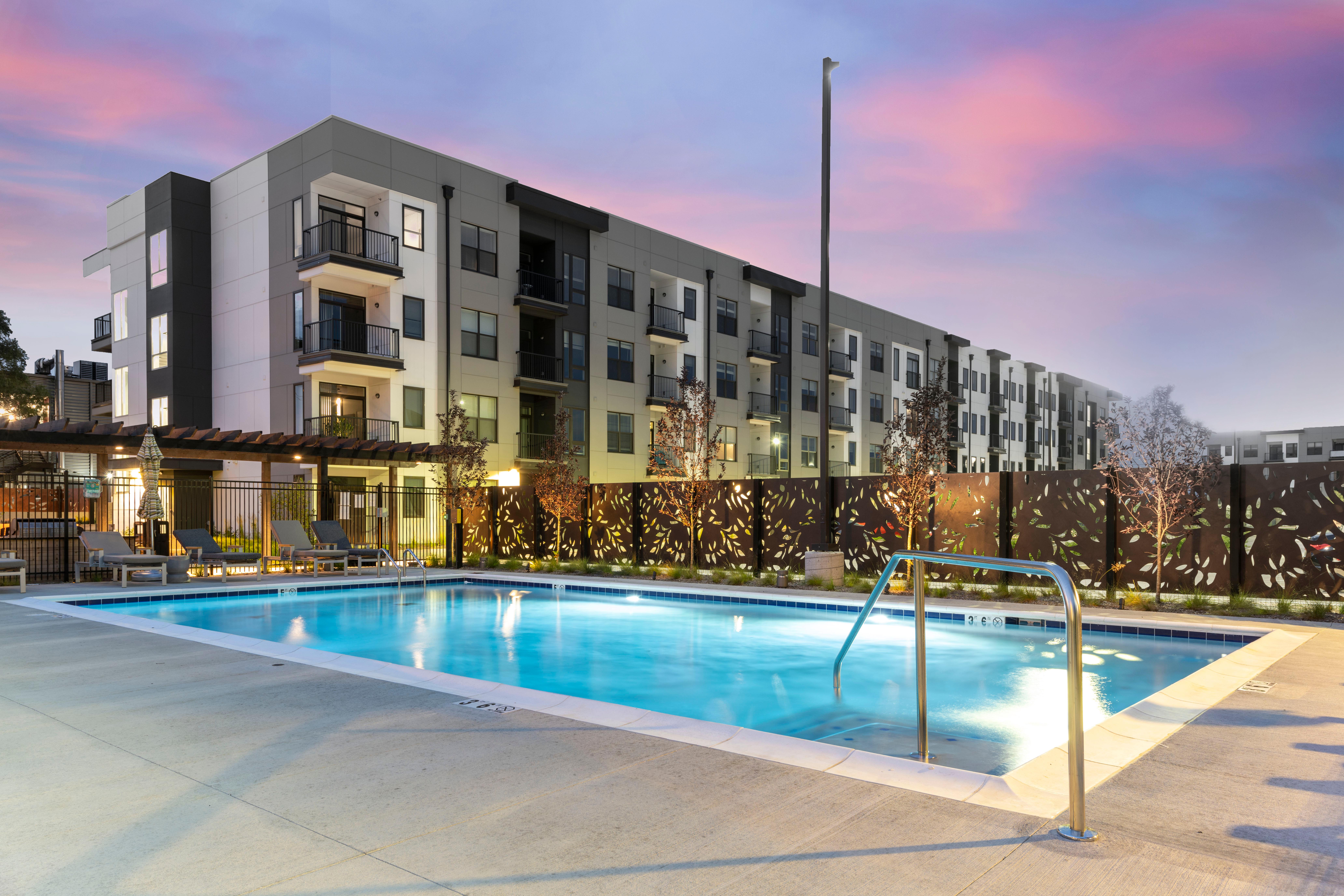 Apartment Complex Pool at Dusk Modern apartment complex with a swimming pool at dusk, featuring lounge chairs and decorative fencing.