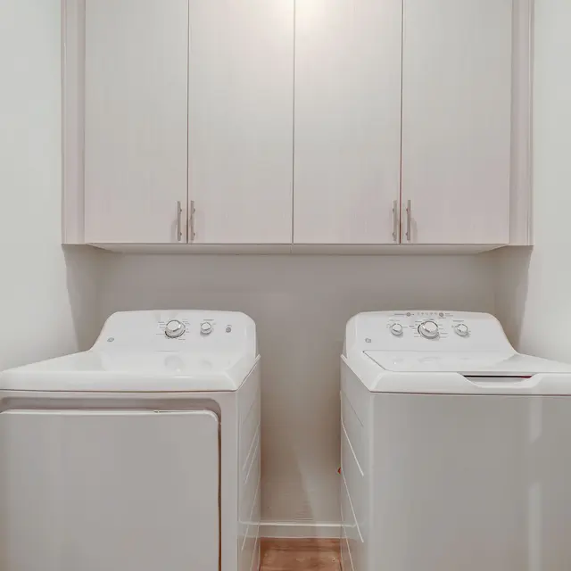 A laundry room featuring a washer and dryer side by side with white cabinetry above and a light-colored wall.