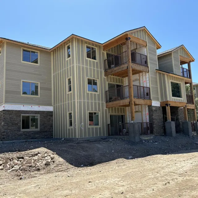 New Apartment Complex Under Construction A two-story apartment building under construction with a mix of siding and stone exterior. The building features multiple balconies and large windows. The site is bare and includes some dirt and construction materials.