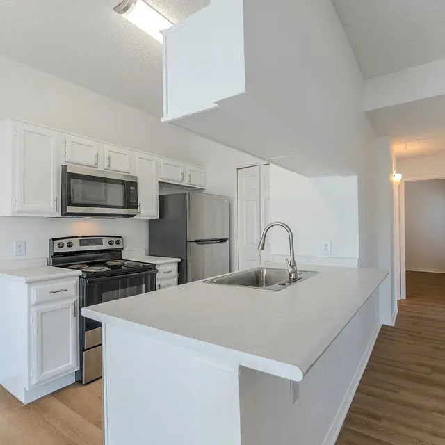 A modern kitchen featuring white cabinetry, stainless steel appliances, and a spacious layout with wood flooring.