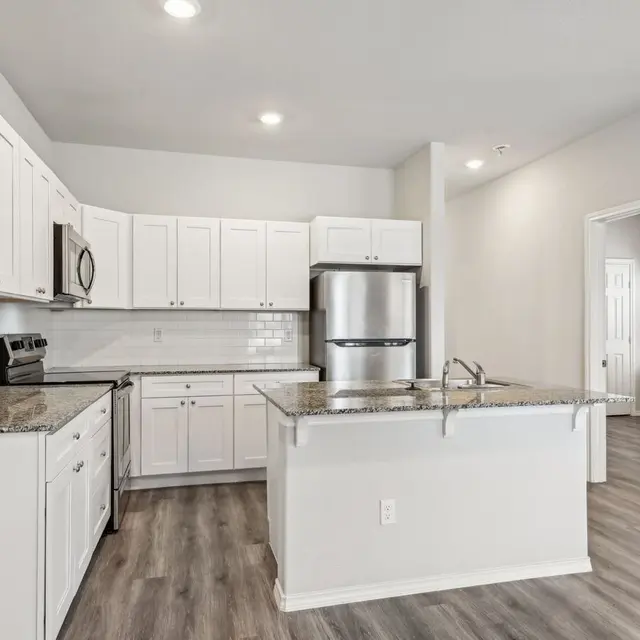 A modern kitchen featuring white cabinets, stainless steel appliances, and granite countertops. The kitchen includes a center island and is well-lit with recessed lighting.