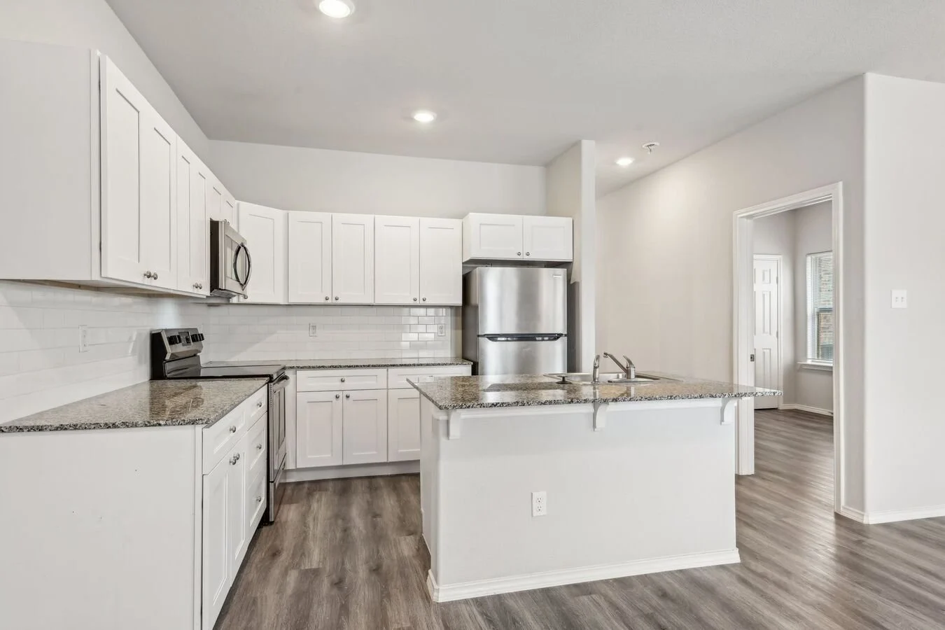 A modern kitchen featuring white cabinets, stainless steel appliances, and granite countertops. The kitchen includes a center island and is well-lit with recessed lighting.