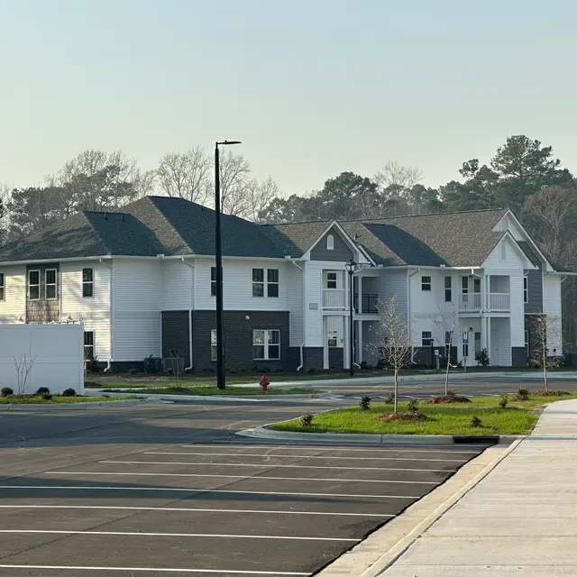 A new apartment complex with a combination of white and gray exteriors, surrounded by a paved parking area and green landscaping.
