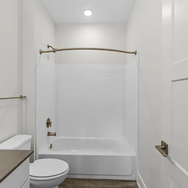 A modern bathroom featuring a white bathtub with a shower curtain, a toilet, a sink with a countertop, and beige walls.