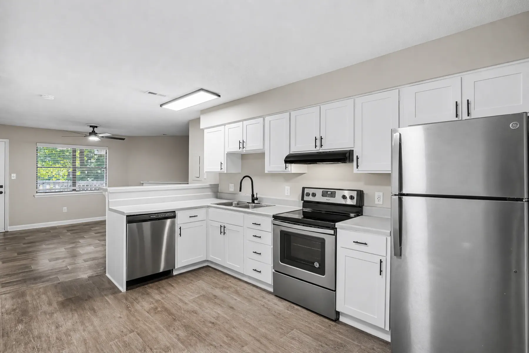 A modern kitchen with white cabinets, stainless steel appliances, and wooden flooring.