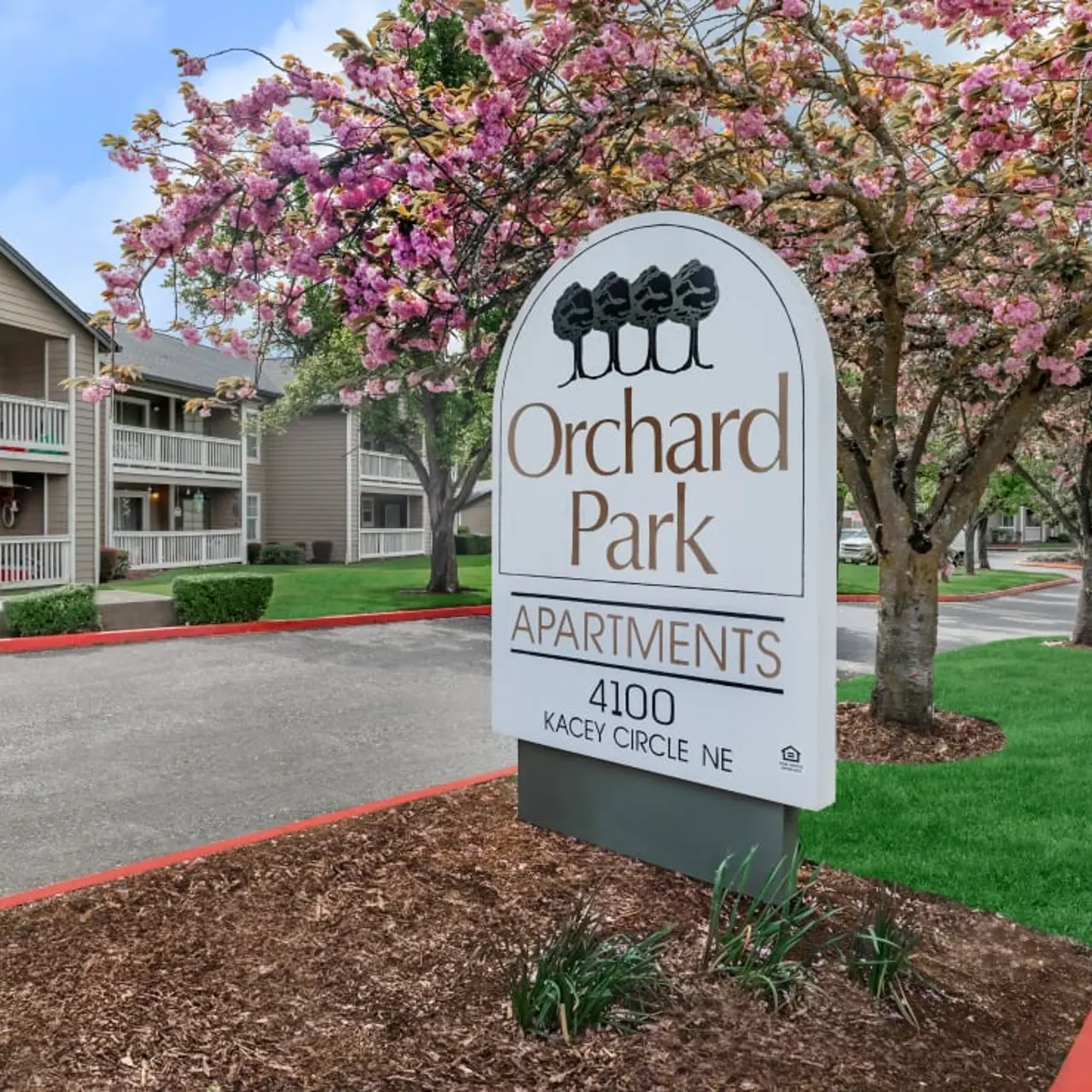Sign for Orchard Park Apartments surrounded by blooming cherry blossom trees and well-maintained landscaping.