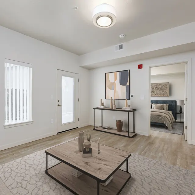 A modern living room with light-colored walls, a small coffee table, and a sofa. There are decorative elements on a console table, with a doorway leading to another room.