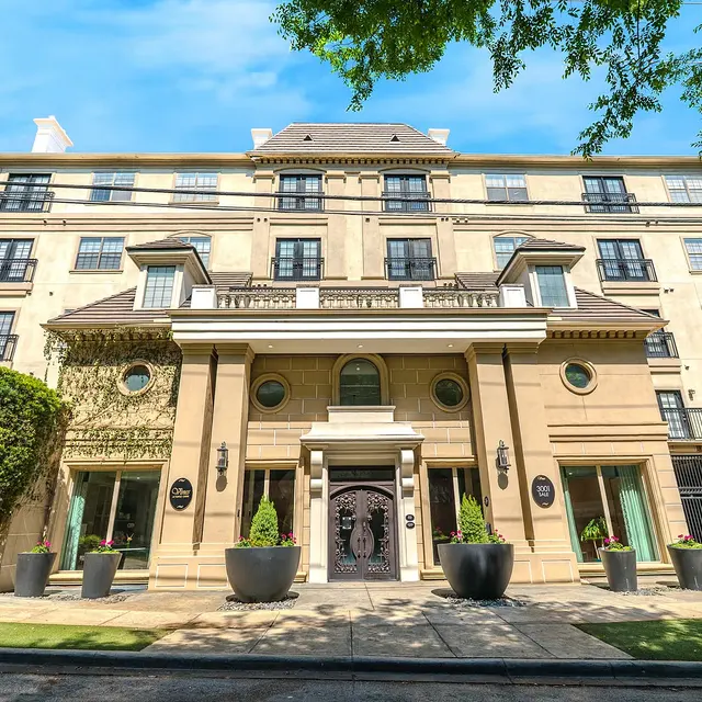 Front view of a historic building with intricate architectural details, large planters, and greenery.