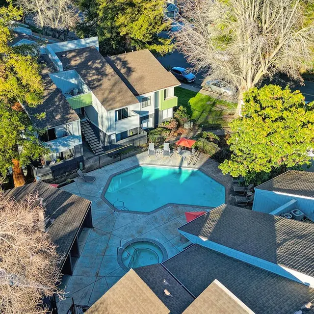Aerial view of a residential property featuring a swimming pool, surrounded by trees and different buildings.