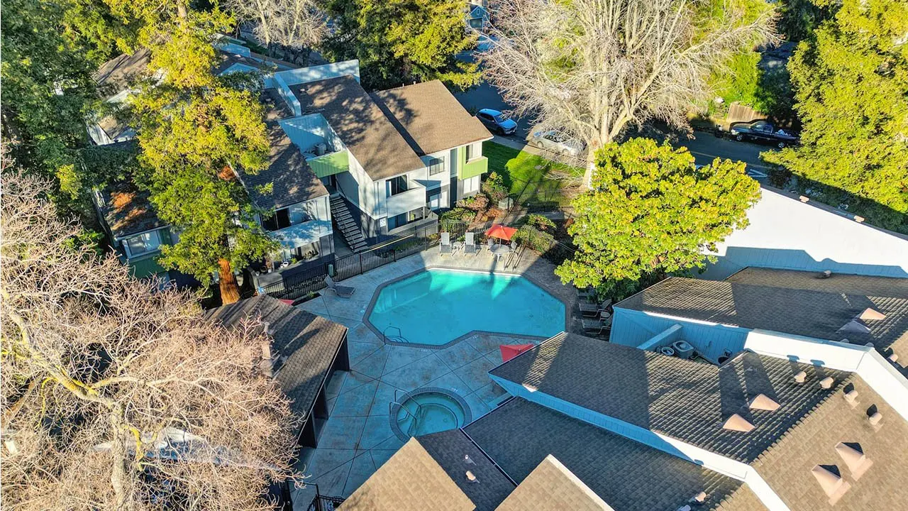 Aerial view of a residential property featuring a swimming pool, surrounded by trees and different buildings.