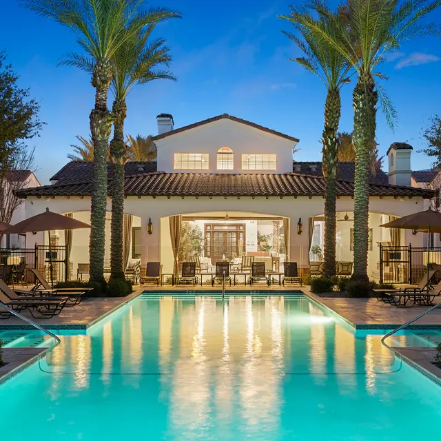 A beautiful outdoor pool area with lounge chairs and palm trees, surrounded by a modern building at dusk.