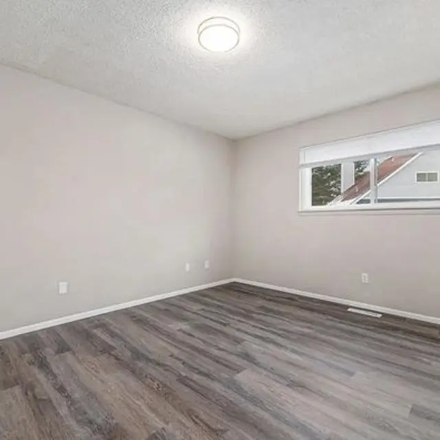 An empty room with light-colored walls and a large window.
