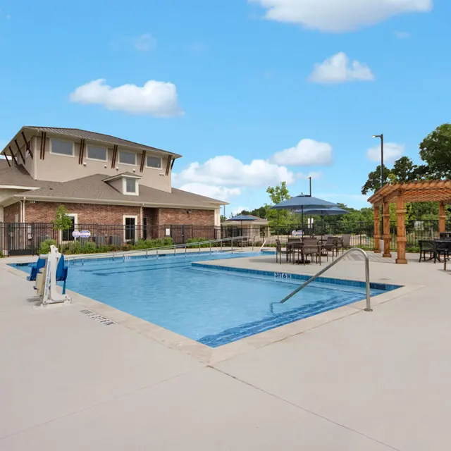 Apartment Complex Pool Area A spacious pool area at an apartment complex featuring a clear blue water pool, lounge chairs, and a wooden pergola set against a clear blue sky.