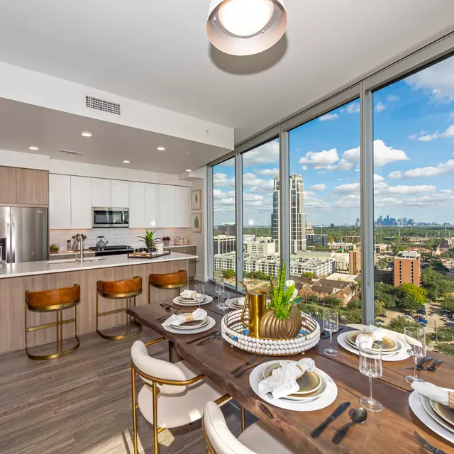 A modern apartment interior with a dining area and a view of the city skyline.