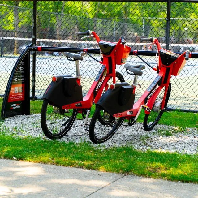 Two red bicycles parked next to a fence, with a sign for bicycle rentals in the foreground.
