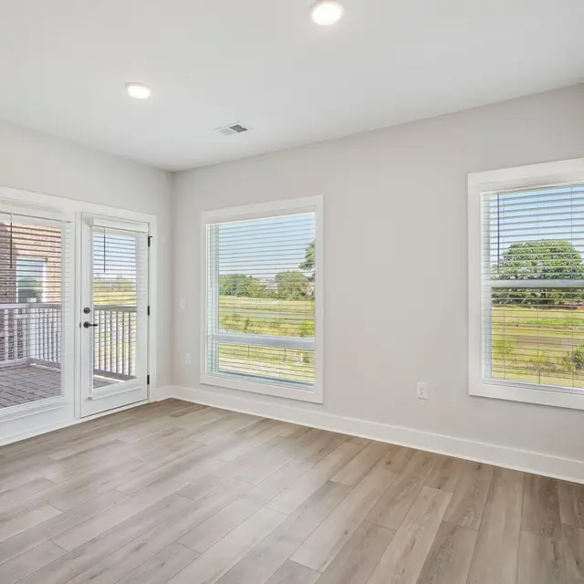 A bright room featuring large windows and wooden flooring, with a door leading outside.
