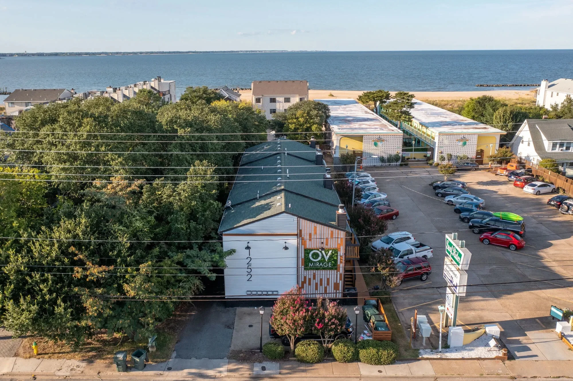 Aerial view of a coastal community with buildings, parking lot, and sea in the background.