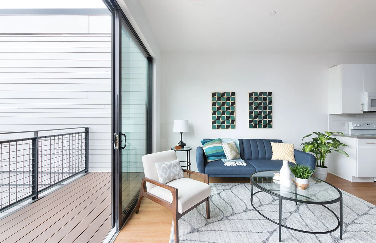 Modern Living Room with Balcony A modern living room featuring a blue sofa, a glass coffee table, and a view of a balcony through large sliding doors.