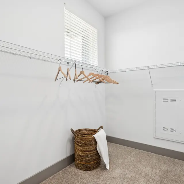 Modern Walk-In Closet A spacious walk-in closet with wire shelving and wooden hangers. A wicker basket is placed on the floor, and there are windows letting in natural light.