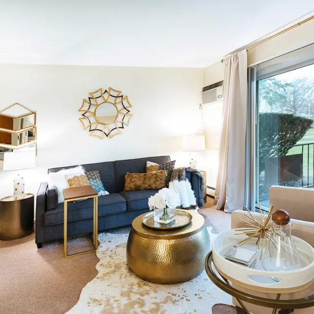 A stylish modern living room featuring a navy blue sofa, gold-accented coffee table, and large windows with outdoor views.