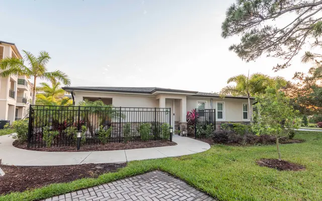 Ground Level Property with Lush Landscaping Exterior view of a fenced property with landscaping and pathways, featuring palm trees and a well-maintained garden