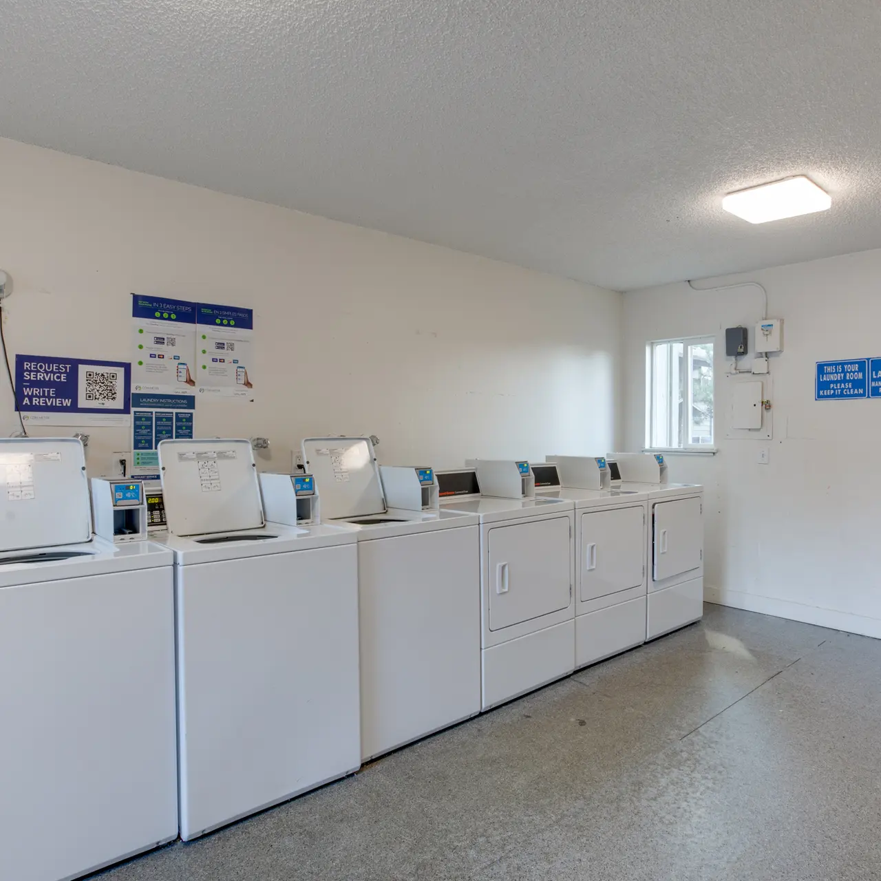 Laundry Room Interior A clean, bright laundry room with several white washing machines lined up against a white wall. There are also signs on the wall providing information about the facility.