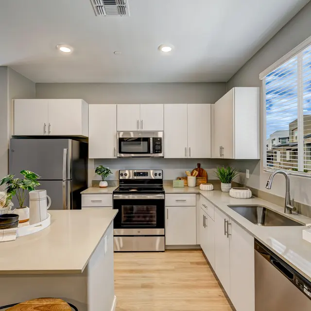 Town Germann - Kitchen Modern kitchen with stainless steel appliances, white cabinets, light countertops, and a view out of a window.