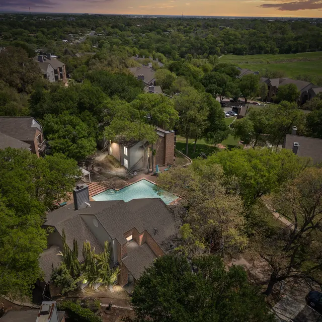 Aerial view of an apartment complex with a swimming pool surrounded by trees and green areas.