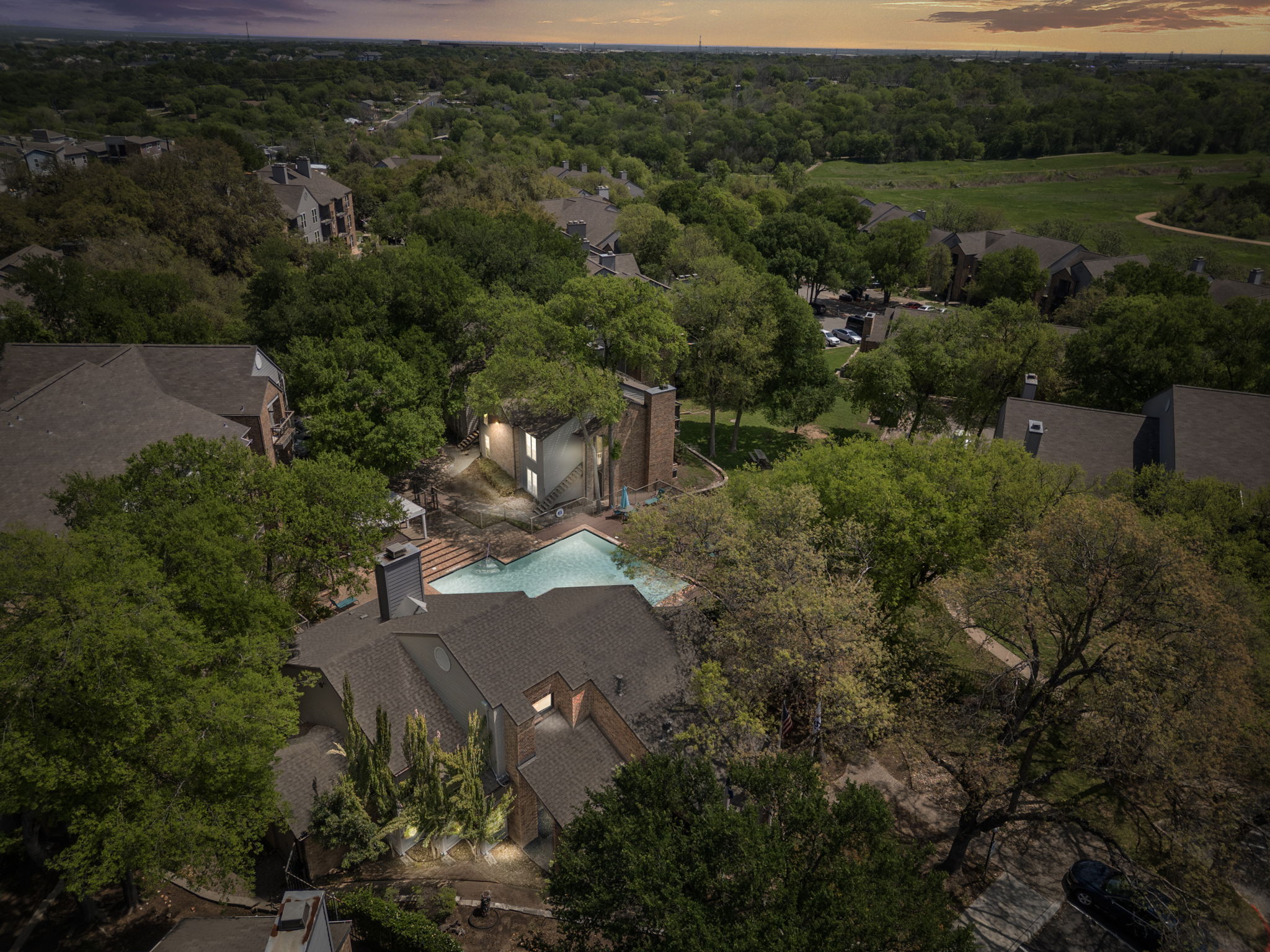 Aerial view of an apartment complex with a swimming pool surrounded by trees and green areas.