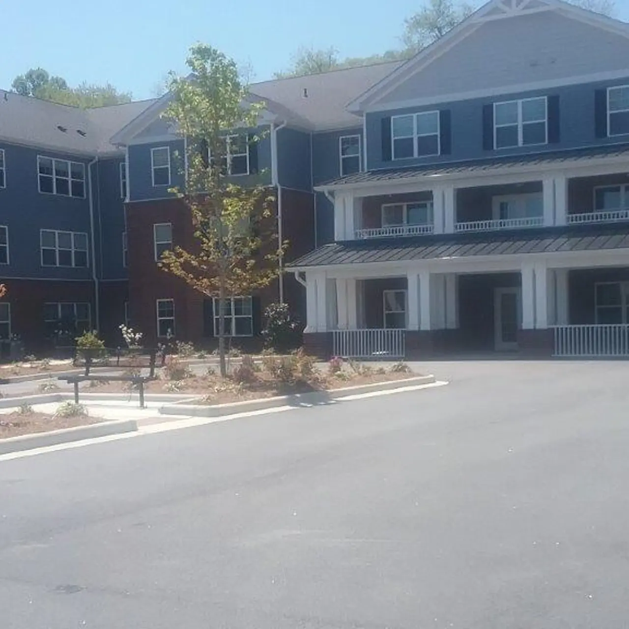 A new apartment complex featuring multiple buildings with brick exteriors, a paved entrance, and landscaped gardens. The central building has a porch and balconies.