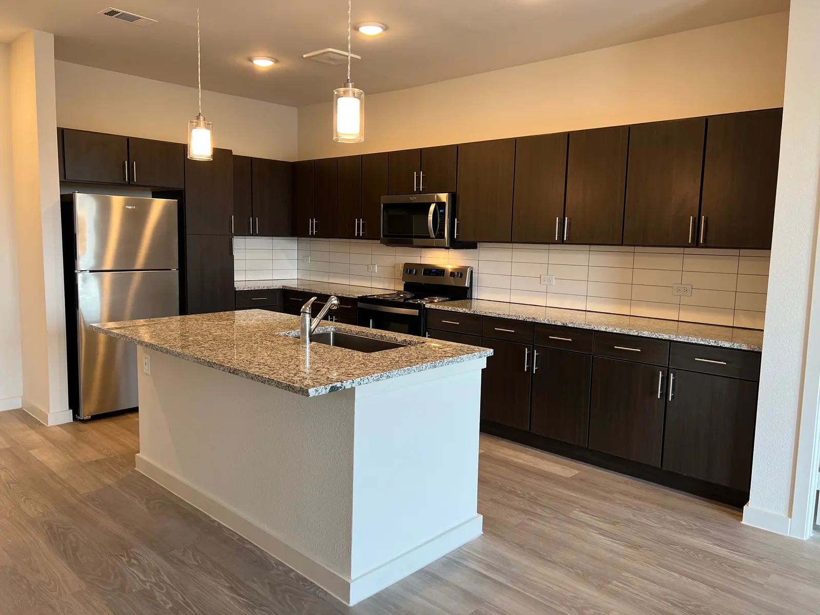 A contemporary kitchen featuring dark wooden cabinets, stainless steel appliances, and a large granite island with a sink.