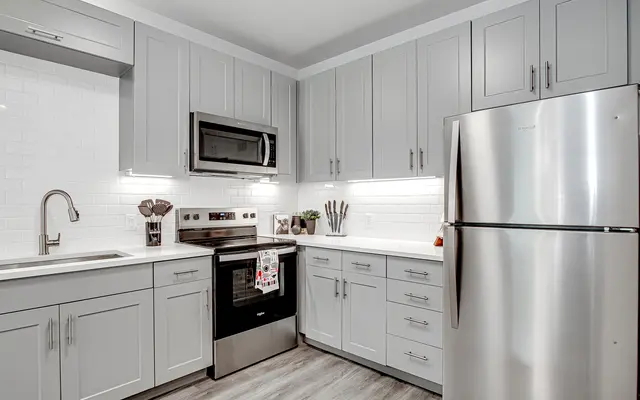 A modern kitchen featuring gray cabinets, stainless steel appliances including an oven and refrigerator, and a minimalist decor style with wooden flooring.